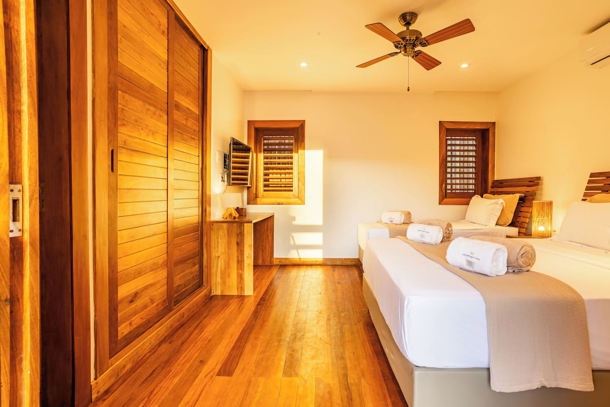 A bedroom with wooden flooring, a bed with white linens, a wooden wardrobe, and a ceiling fan.
