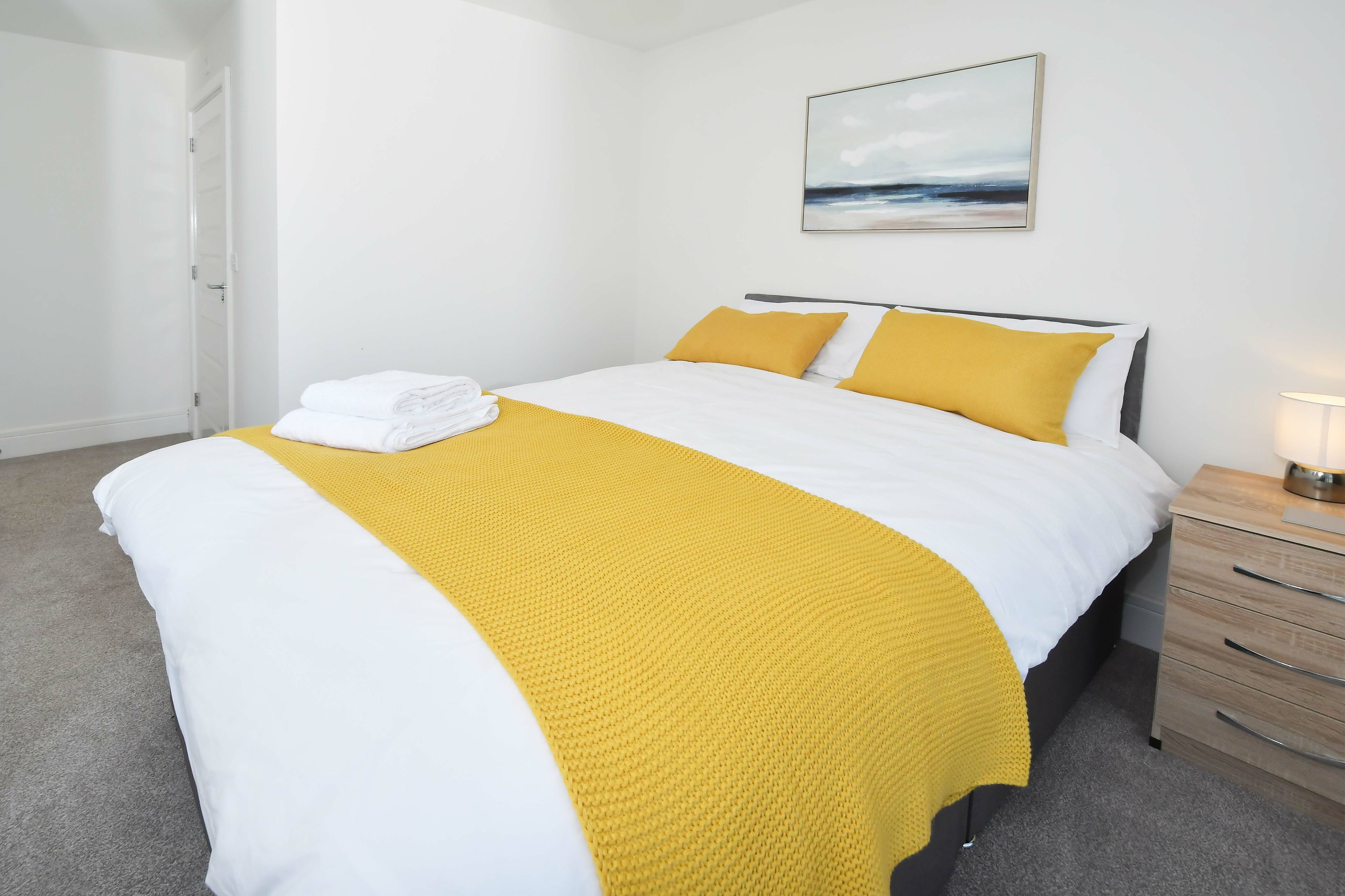 A neatly made bed with white and yellow bedding, a single yellow throw blanket, and a folded white towel on the foot of the bed.