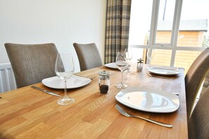 Mesa de jantar posta para quatro pessoas, com pratos brancos, copos de vinho e talheres.
