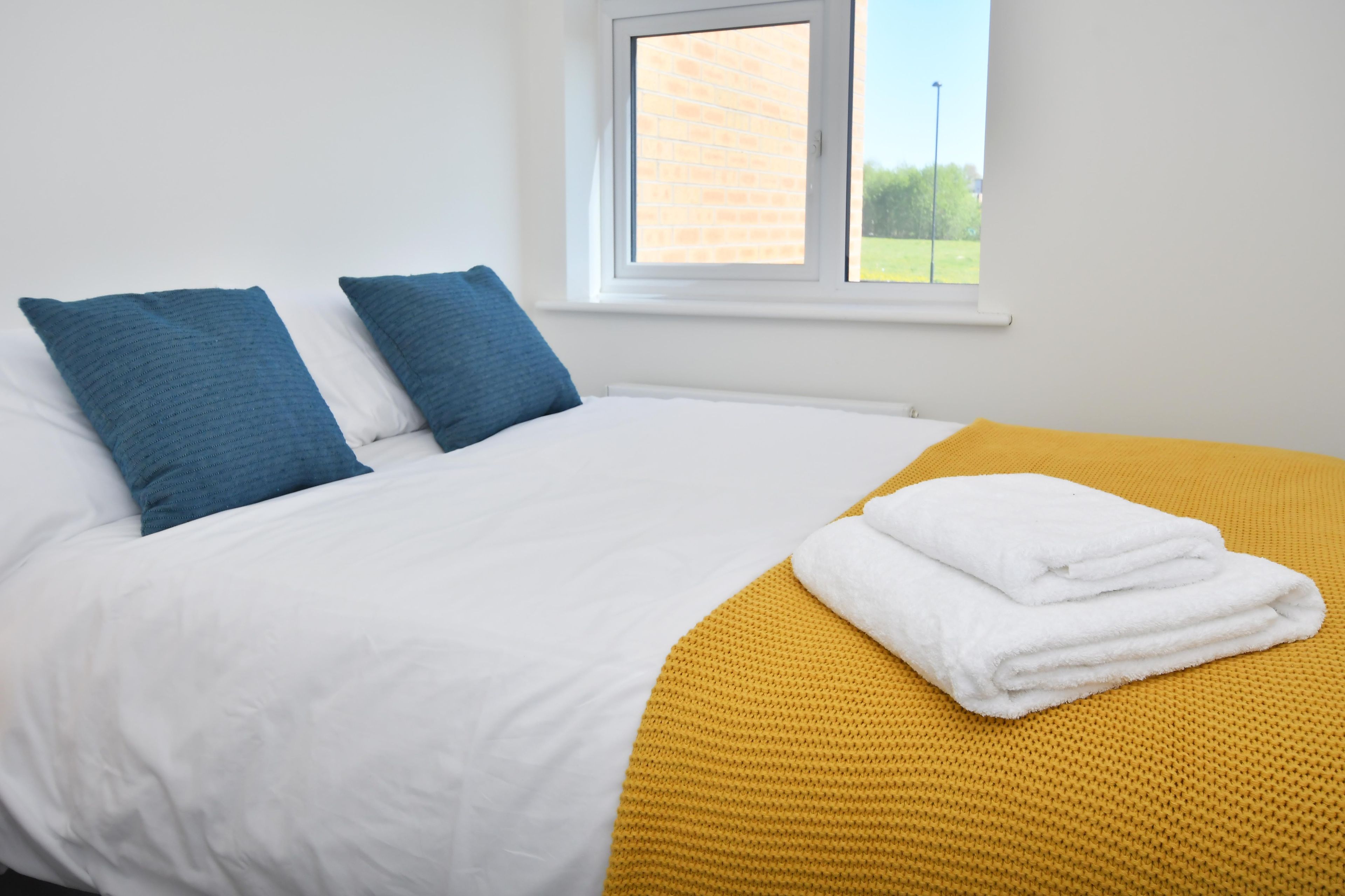 A bed with white bedding and blue pillows, a yellow throw blanket, and a white towel.