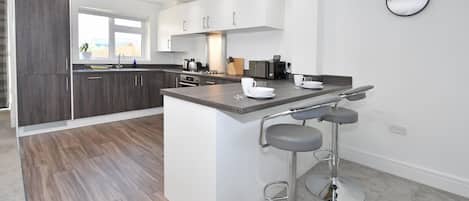 A modern kitchen with a central island, bar stools, and a wall-mounted clock.