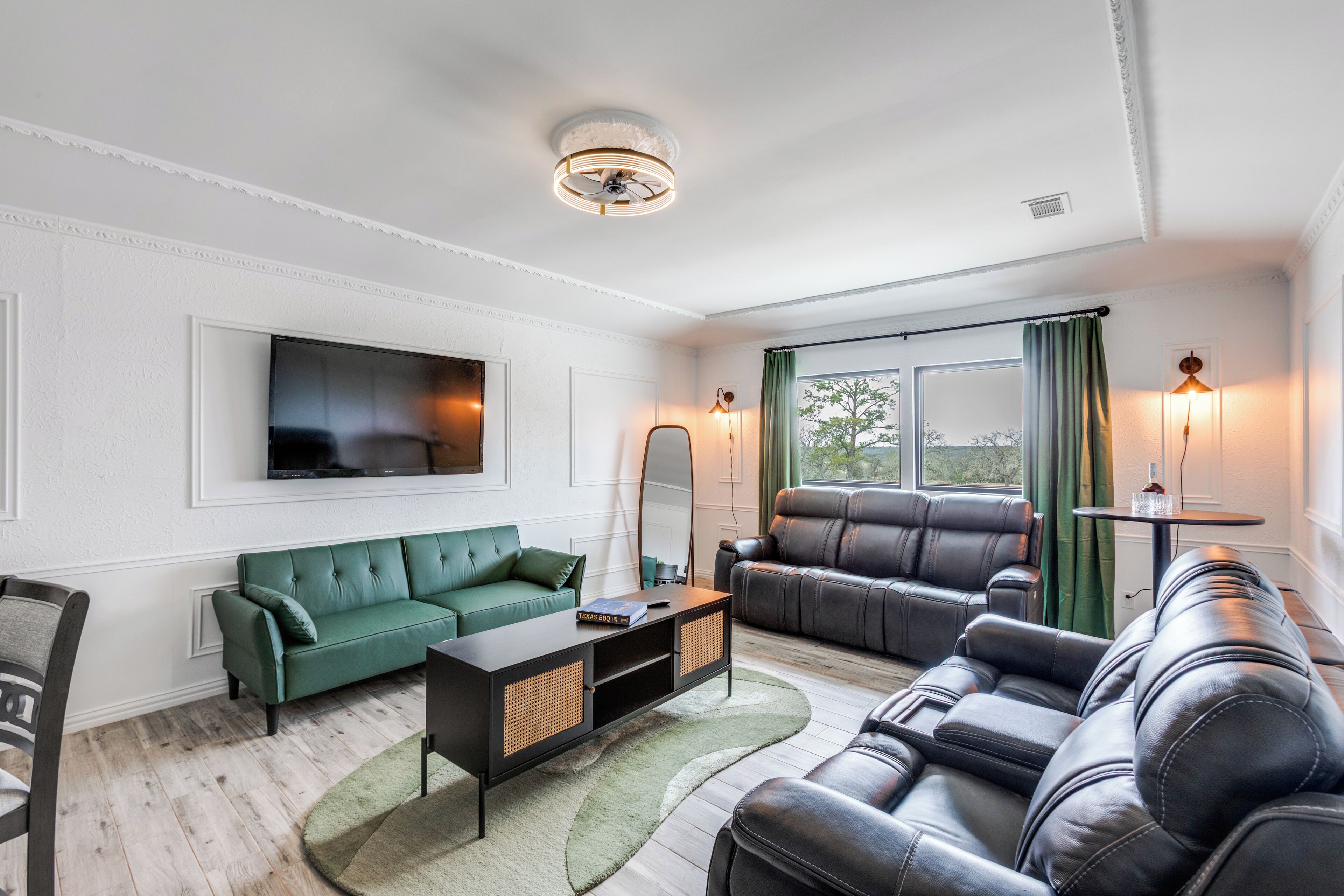 Un salon moderne avec un canapé vert, un divan en cuir noir et un téléviseur à écran plat fixé au mur.