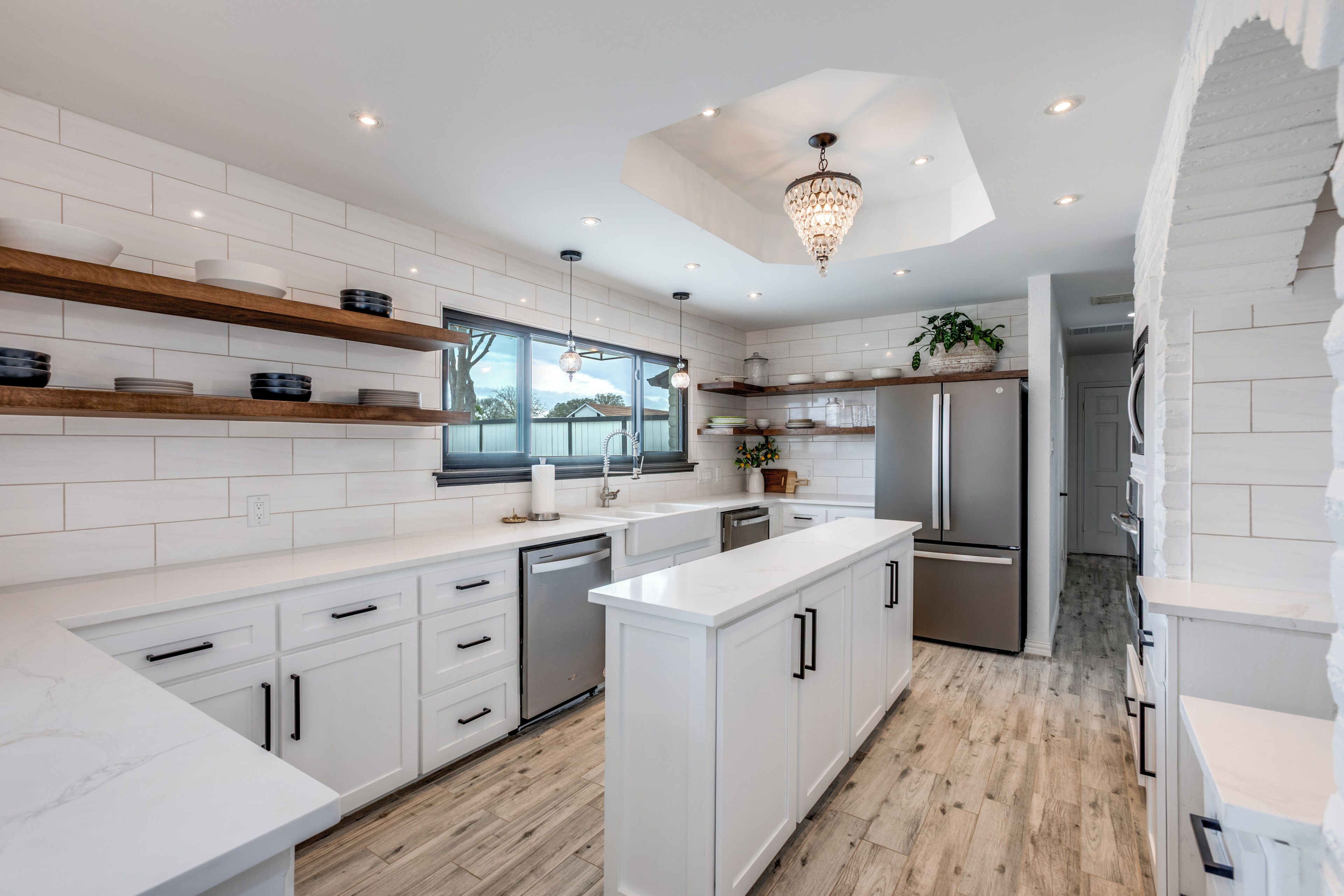 Une cuisine moderne avec des meubles blancs, des étagères en bois et un îlot central.