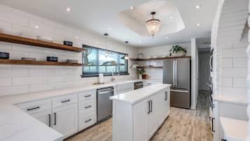 Une cuisine moderne avec des meubles blancs, des étagères en bois et un îlot central.