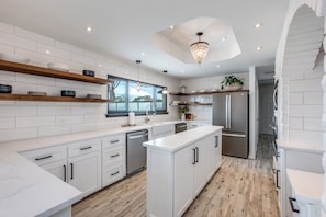 Une cuisine moderne avec des meubles blancs, des étagères en bois et un îlot central.