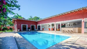 A swimming pool with a red building in the background. - Mansion for up to 28 people on Pernambuco Beach - 350m from the sea - air conditioning (Guarujá)