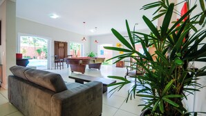 A spacious living area with a sofa, a dining table, and a potted plant. - Mansion for up to 28 people on Pernambuco Beach - 350m from the sea - air conditioning (Guarujá)