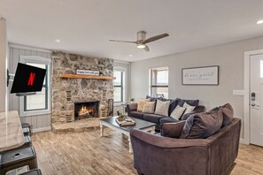 Un salon doté d’une cheminée en pierre, d’un téléviseur à écran plat, d’un ventilateur de plafond et d’un coin salon confortable.
