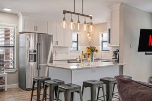 Une cuisine moderne dotée d’un réfrigérateur en acier inoxydable, d’un îlot central avec des tabourets de bar et d’un luminaire suspendu.