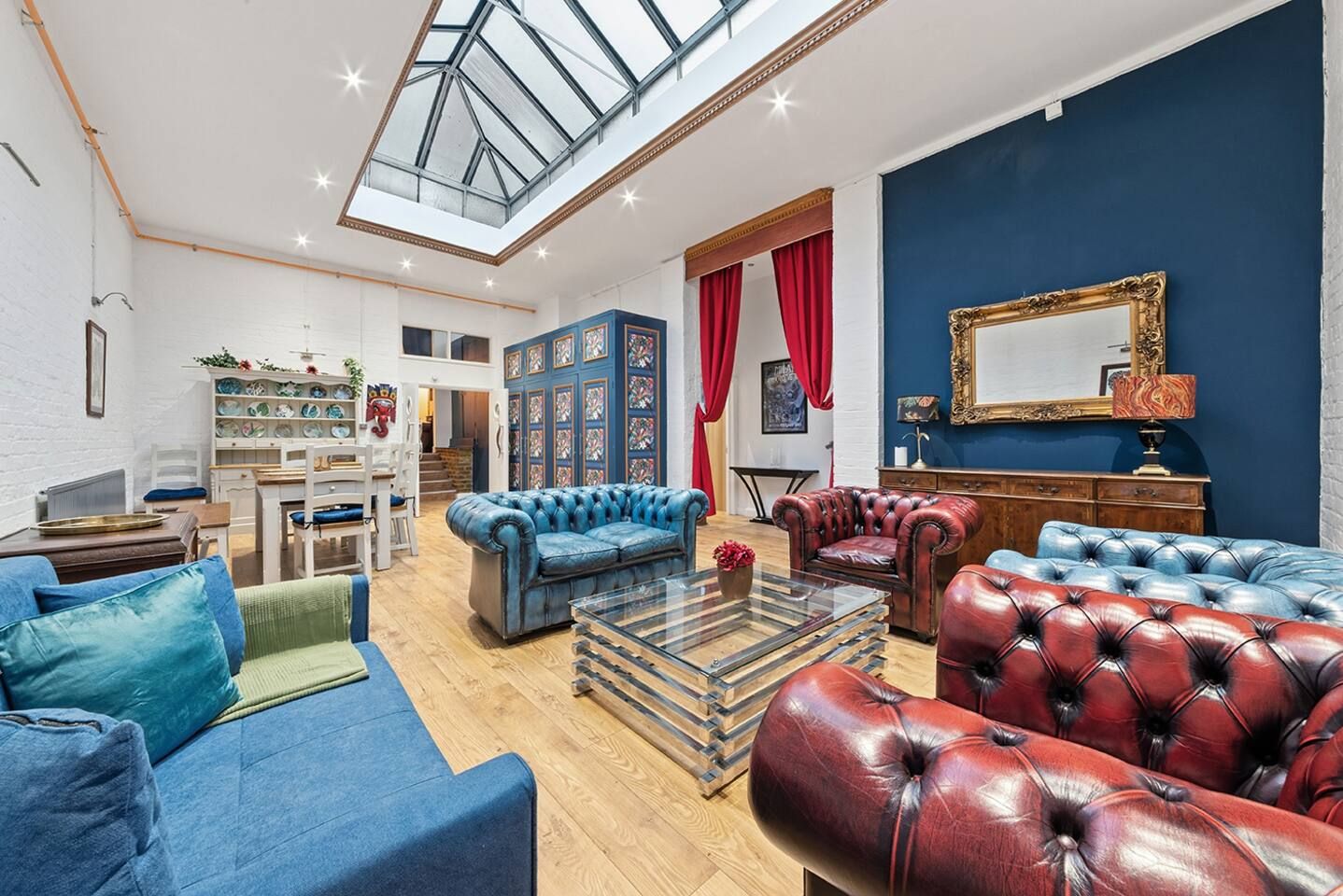 A spacious living room with leather sofas, a glass coffee table, and a high ceiling with skylight.