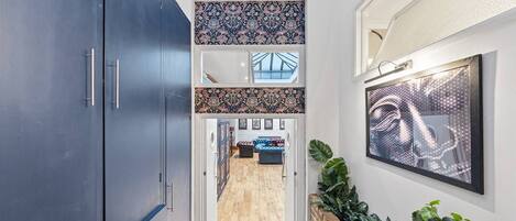 Un couloir avec une armoire bleu foncé, des carreaux muraux à motifs, un plancher en bois, un coin salon avec un canapé bleu et une œuvre d’art encadrée.