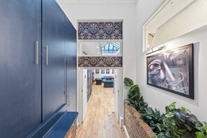 A hallway with a dark blue cabinet, patterned wall tiles, a wooden floor, a seating area with a blue sofa, and a framed artwork. - Royal College St NW1, Camden Town, Camden Rd (London)