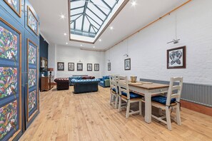 A room with a wooden floor, a blue sofa, a dining table with chairs, and a skylight. - Royal College St NW1, Camden Town, Camden Rd (London)