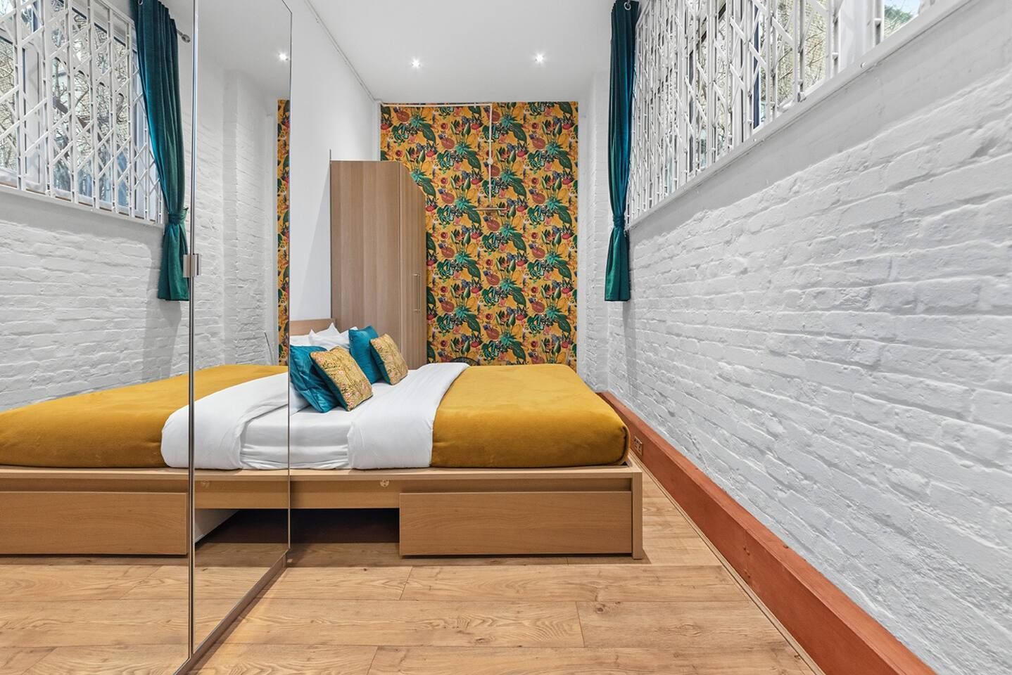 Une chambre moderne avec un lit en bois, une literie blanche et un papier peint à motifs floraux colorés.