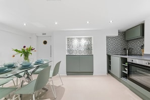 A modern kitchen with a dining area, featuring a glass table, chairs, and a vase with flowers. - Royal College St NW1, Camden Town, Camden Rd (London)