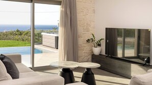 A modern living room with a large TV, comfortable seating, and a view of the ocean. - Luxurious Villa Rocca Blanco 2 (Chania)