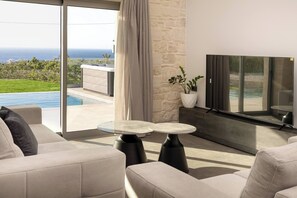 Ein modernes Wohnzimmer mit großem Fernseher, bequemen Sitzgelegenheiten und Blick aufs Meer.