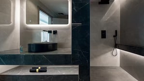 A modern bathroom with a large mirror, a round sink, and a shower area. - Luxurious Villa Rocca Blanco 2 (Chania)