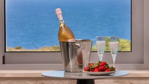 A champagne bottle in a metal bucket, two glasses, and a plate of strawberries on a table by a window with a view of the ocean. - Luxurious Villa Rocca Blanco 2 (Chania)