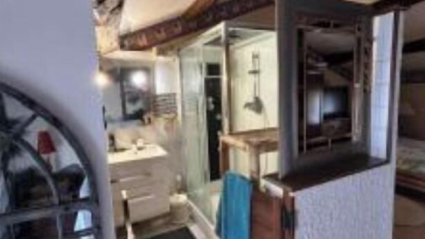 Un baño moderno y compacto con cabina de ducha de vidrio, tocador de madera y toallero visible.