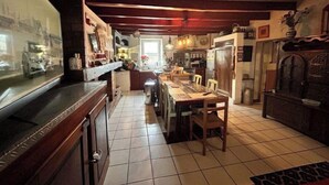 Una cocina con una encimera larga, una mesa de comedor y sillas. Incluye un refrigerador, un lavamanos y diversos electrodomésticos.