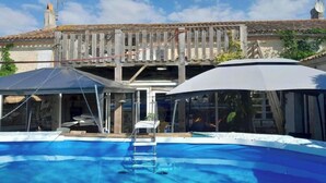 Una piscina con plataforma de madera y zona de estar cubierta.