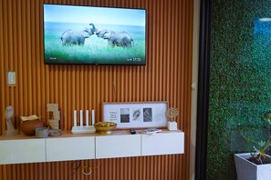 Ein an der Wand montierter Fernseher zeigt eine Elefanten Szene, ein gerahmtes Bild und eine weiße Konsole mit Dekorationen.