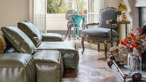 A room with a large window, a green sofa, a blue chair, a small table, and a fireplace. - Eccleston Square V by onefinestay (London)