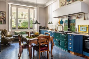 A dining area with a table and chairs, a kitchen with blue cabinets and a stove, and a large window with a view of greenery. - Eccleston Square V by onefinestay (London)