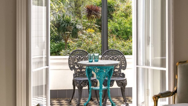 An open doorway leading to a garden with a table and chairs, a lamp, and a sofa inside. - Eccleston Square V by onefinestay (London)