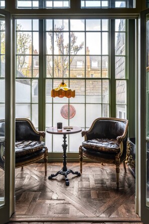 A room with a large window, two upholstered chairs, a small round table, and a floor lamp. - Eccleston Square V by onefinestay (London)