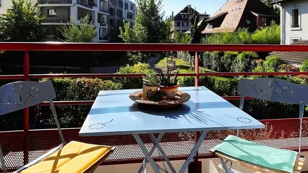 Una terrazza all'aperto con tavolo e sedie, un tendaggio a righe rosse e gialle e vista sugli edifici sullo sfondo.