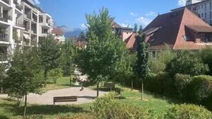 Un parco con panchine e alberi, circondato da edifici con balconi e una montagna sullo sfondo.
