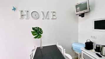 A room with a dining table, a clock, a TV, and a microwave.