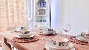 Una mesa de comedor dispuesta con platos, tazones y cubiertos blancos, individuales tejidos y cristalería.