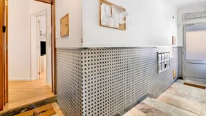 Un pasillo con una recepción, una puerta de madera, un teléfono en la pared y un tablón de anuncios.