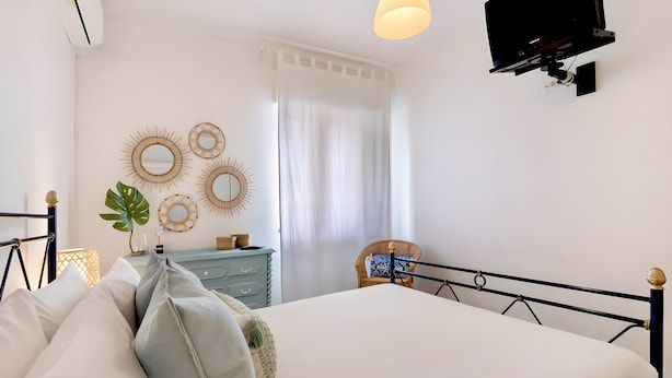 Un dormitorio con cama, mesitas de noche, cómoda, silla y espejos en la pared.
