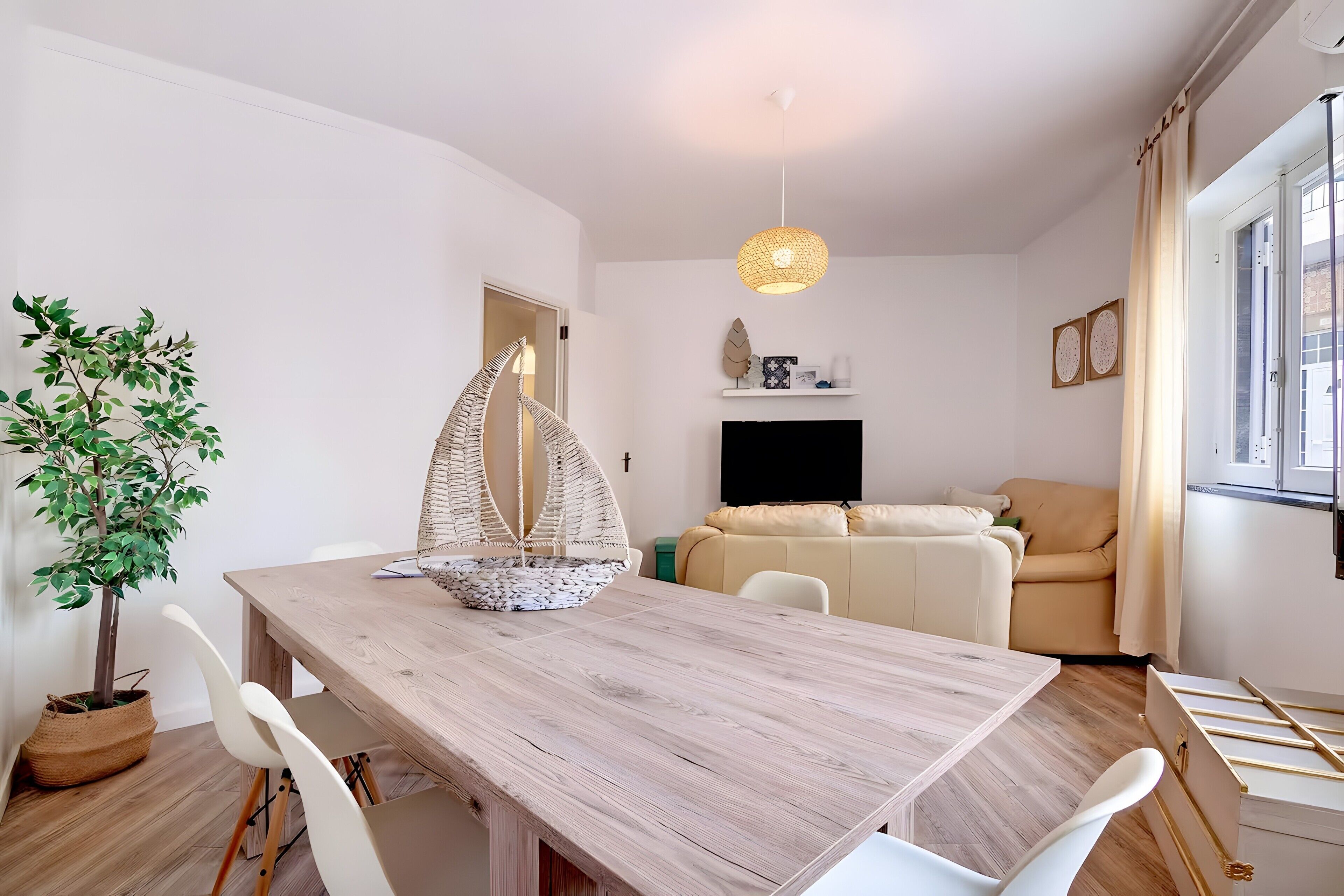 Ein zeitgemäßer Wohnraum mit einem Holzesstisch, weißen Stühlen, einem Hängesessel, einer Couch und einem Fernseher.