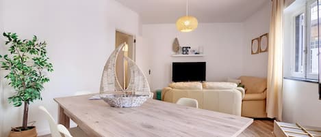 Un espace de vie moderne comprenant une table à manger en bois, des chaises blanches, un fauteuil suspendu, un canapé et un téléviseur.