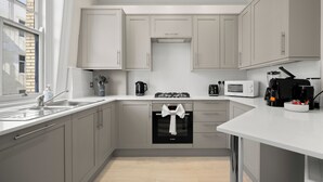 Een moderne keuken met grijze kastjes, een inbouwoven, een magnetron en een koffiezetapparaat.