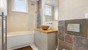 Een badkamer met een badkuip, douche, wastafel, spiegel en raam.