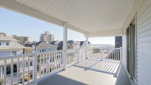 Een overdekt balkon met witte leuningen, met uitzicht op een woongebied met huizen en een gebouw in de verte.