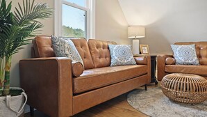 A brown leather sofa with patterned cushions, a wicker ottoman, and a potted plant in a woven basket. - Delightful Appalachian Trail 2-bedroom lodge with AC in Central Damascus (Damascus)