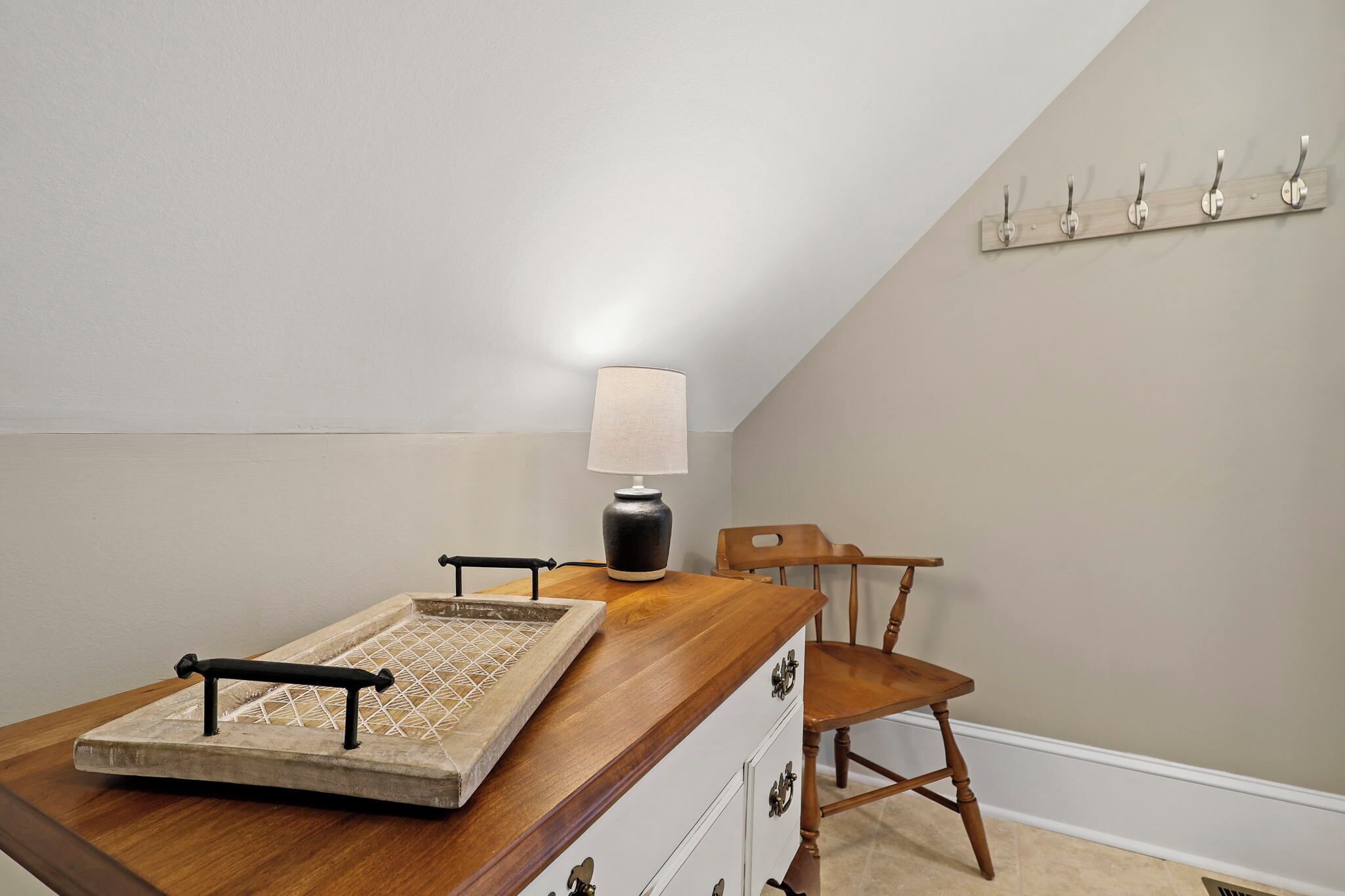Une pièce comprenant un bureau en bois, une lampe, une chaise et un porte-manteau.