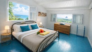 Ein Schlafzimmer mit Bett, Nachttischen, einem Schminktisch und Blick auf den Ozean.