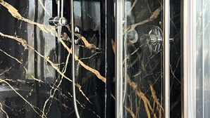Un baño con pared de mármol negro y mampara de vidrio.