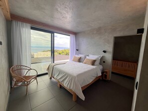 A bedroom with a bed, a chair, a nightstand, and a view of the outdoors.