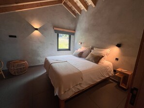 A bedroom with a bed, bedside tables, a window, and a woven stool.