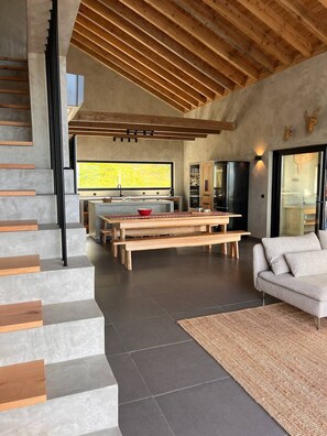 A modern kitchen with a large window, a dining area with benches, and a staircase with wooden steps.
