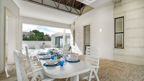 A dining area with white tables and chairs, a view of the outdoors, and a stone floor. - Very beautiful villa a few steps from the beach (Marina di Ragusa)